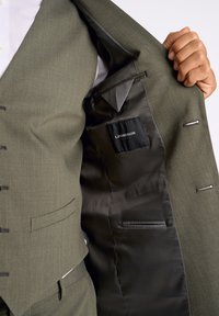 Olijfgroene blazer met een gladde zwarte satijnen voering. Bevat een binnenzak met een label, gestructureerd ontwerp en zijzakken.