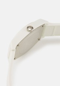 Montre en plastique blanc avec un boîtier rectangulaire, une quincaillerie en argent brossé, un bracelet texturé et un dos lisse et métallique.