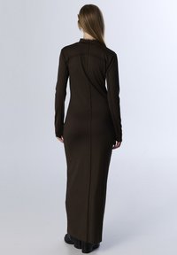 Lange bruine jurk van gladde stof, met lange mouwen, een aansluitende pasvorm en een rits aan de achterkant. Minimalistisch ontwerp zonder zichtbare patronen.