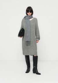 Siva pletena obleka s dolgimi rokavi, do kolen, v kombinaciji s svetlo sivo šal, črno torbico in črno visoko peto čevljev.