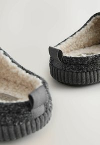 Grå stof slippers med et blødt, fuzzy indre, der har en tekstureret yderside og små løkkeaccenter på hælen.