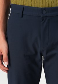 Mørkeblå bukser med en glat tekstur, der har knaplukning, bæltestropper og et slankt fit design. Professionel og alsidig i stilen.