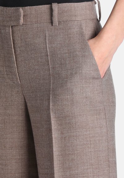 Gros plan d'une personne portant un pantalon marron texturé avec une main placée dans la poche avant.