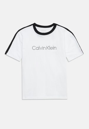 T-shirt blanc à manches courtes avec col noir et bandes noires sur les épaules, arborant le logo "Calvin Klein" en texte noir pointillé sur la poitrine.