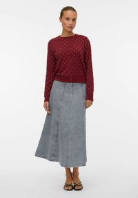 Cárdigan burdeos con lunares blancos, escote redondo y cierre de botones, combinado con una falda larga de denim gris claro.