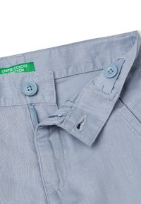 Světle modré bavlněné kalhoty s zipem, dvěma knoflíky a štítkem s nápisem "UNITED COLORS OF BENETTON." Hladká textura a upravený design.