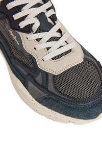 Sneaker grigio e navy con tessuto in rete, dettagli in suede e lacci bianchi. Presenta texture a contrasto e una suola spessa e maculata.