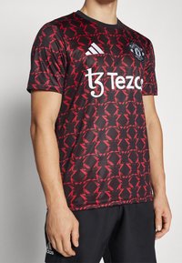 Musta jalkapallopaita, jossa punainen geometrinen kuvio, valkoisella logolla ja tekstillä. Lyhyet hihat ja pyöreä kaulus. Valmistettu synteettisestä kankaasta.