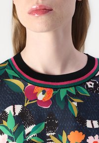 Floral-patterned top with a black ribbed collar featuring pink and green accents. Fabric has a smooth texture with vibrant colors and detailed designs.