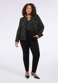Schwarze Tweedjacke mit mehrfarbigen Nähten, cropped Design, fransigen Kanten. Kombiniert mit schwarzen Hosen und spitzen schwarzen Absätzen.