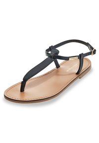 Sandalo in pelle nera con suola piatta color tan e un'unica cinghia alla caviglia con fibbia dorata. Texture liscia con minimi dettagli di cucitura.