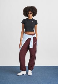 Čierne skrátené tričko s logom Nike, bordové športové nohavice so bočnými pruhmi, modrý sveter zviazaný okolo pása a biele športové topánky.