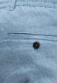 Κοντινή λήψη ανοιχτό μπλε υφασμάτινου παντελονιού με πίσω τσέπη με κουμπί και εμφανείς ραφές.