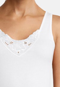 White tank top with a V-neckline featuring embroidered floral lace detailing around the edge. Smooth texture. No additional patterns or accents.