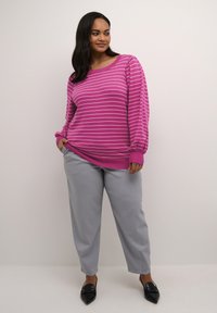 Rosa gestreifter Pullover mit langen Ärmeln und gerippten Bündchen, kombiniert mit hellgrauen Hosen. Schwarze Schuhe mit spitzer Zehe.