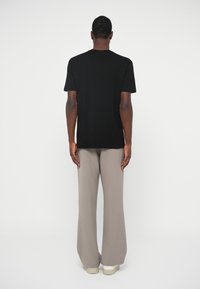 Μαύρη κοντομάνικη μπλούζα με στρογγυλή λαιμόκοψη, συνδυασμένη με ανοιχτό μπεζ παντελόνι με φαρδιά πόδια και λευκά αθλητικά παπούτσια. Μινιμαλιστικός σχεδιασμός.