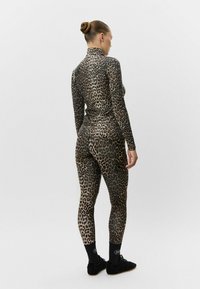 Conjunto de body de estampado de leopardo en tonos marrón y negro, con un collar alto, mangas largas y leggings ajustados con una textura suave. Zapatillas deportivas negras.