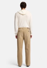 Pantaloni di cotone beige con una vestibilità rilassata, dotati di due tasche posteriori e un'etichetta in vita, abbinati a una felpa leggera color crema.