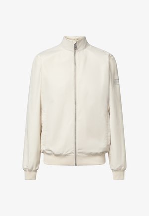 Chaqueta off-white con cremallera, cuello alto, mangas largas, puños y dobladillo acanalados, y un sutil texto de logo en la parte superior de la manga izquierda.