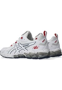 Zapatillas deportivas blancas con un diseño texturizado, que presentan una suela moteada en gris, detalles rojos y un logotipo "GEL" en el lateral.