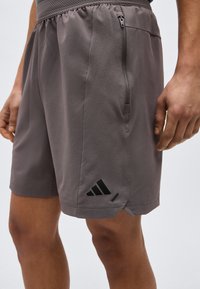 Κοντινή λήψη ενός ατόμου που φοράει γκρι αθλητικές σορτς με φερμουάρ πλαϊνή τσέπη και μαύρο λογότυπο κοντά στο τελείωμα.