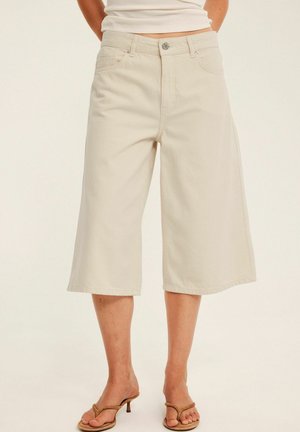 Beige knielange wijde shorts gedragen met bruine sandalen met hak en een cropped witte mouwloze top.