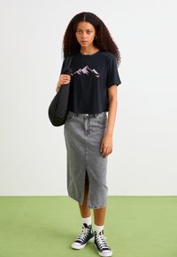 Zwarte cropped t-shirt met een bergafbeelding, gecombineerd met een grijze denim midi rok met een sleuf aan de voorkant. Draag het met zwarte high-top sneakers.