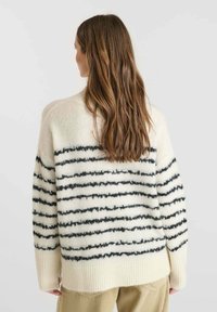 Maglione oversized crema con strisce orizzontali nere, realizzato in materiale morbido e peloso. Le maniche e l'orlo a coste offrono texture e struttura.