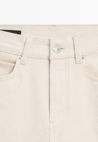 Jeans in denim color avorio a vita alta con bottone frontale visibile, passanti per cintura e tasche anteriori curve con rivetti metallici.