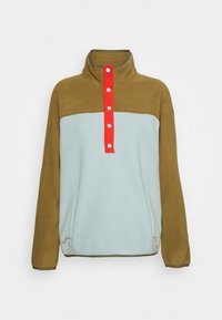 Polarowy półgolf z wysokim kołnierzem, z brązowymi ramionami, jasnoniebieskim korpusem oraz czerwonym rozszerzeniem z białymi guzikami. Dwie boczne kieszenie.