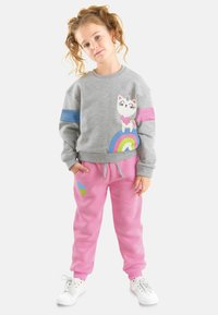 Grå sweatshirt med farverig kattegrafik og regnbue, blå og lyserøde striber. Lyserøde sweatpants med grønne og blå skyaffekter. Hvide sneakers.