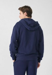 Sweatshirt à capuche bleu marine avec cordon de serrage, poignets et ourlet côtelés ; fabriqué en tissu doux, avec une coupe décontractée et une texture lisse.