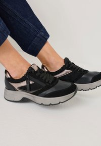 Schwarze und graue Sportschuhe aus einer Kombination von Leder und Wildleder, mit Schnürverschluss, metallischen Akzenten und einer dicken Sohle.