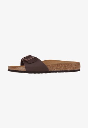 Brown slip-on sandal with a cork footbed, a textured rubber sole, and a wide strap featuring a metallic buckle accent.