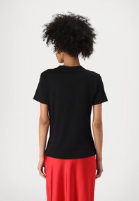 Black short-sleeve t-shirt with a round neckline, smooth fabric, and a straight cut, paired with a flowing red skirt.