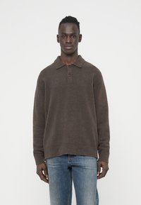 Καφέ πουλόβερ με γιακά, με υφή και τρία κουμπιά. Συνδυασμένο με ανοιχτόχρωμα μπλε τζιν.