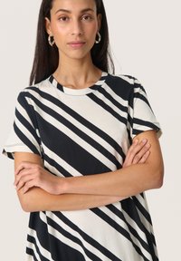 Kortærmet t-shirt med en cremet base og sorte diagonale striber. Blødt stof og en klassisk rund halsudskæring. Ingen bemærkelsesværdige udsmykninger.