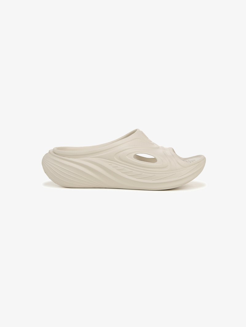 Sabot léger beige avec une surface texturée ondulée, un trou de ventilation ovale, et une forme courbée et ergonomique pour le confort.