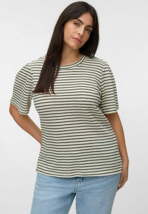 Femme aux longs cheveux foncés portant un haut en maille à manches courtes à rayures crème et noir et un jean bleu clair sur un fond uni.