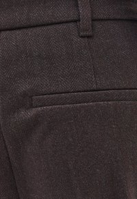 Donkerbruine, op maat gemaakte broek met een visgraatmotief. Voorzien van een vlakke voorkant en een enkele achterzak. Zachte, gestructureerde stof.