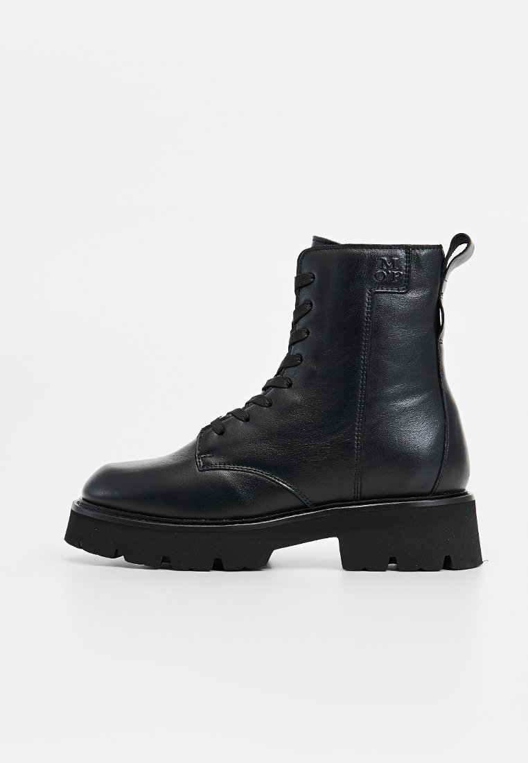 Zwarte leren enkellaars met vetersluiting, ronde neus, chunky zool en een trekbandje aan de hiel. Zijkant heeft stiksels en zichtbaar logo-detail.