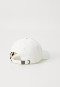 White baseball cap with a curved brim, adjustable strap, and a textured fabric. Features a small logo tag near the adjustment buckle.