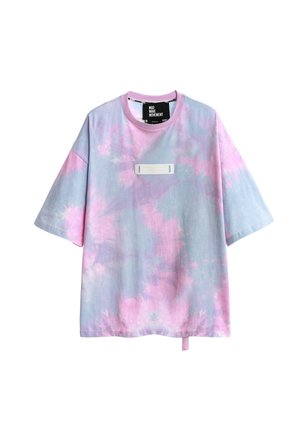 Joven de espaldas con una camisa tie-dye en tonos pastel con alas de lentejuelas de colores, pantalones cortos rojos, calcetines blancos y zapatos beige texturizados.