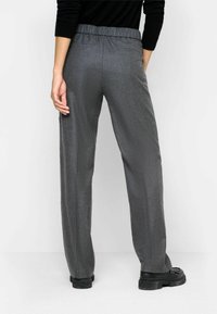 Pantalon gris tissé à coupe décontractée, taille élastique et poches latérales, associé à des chaussures noires épaisses.