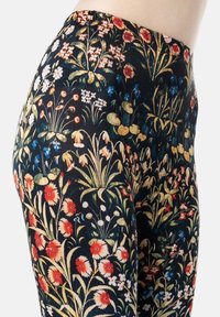Legginsy w kwiaty z czarnym tłem i skomplikowanymi wzorami czerwonych, białych i niebieskich kwiatów; wykonane z elastycznego materiału.