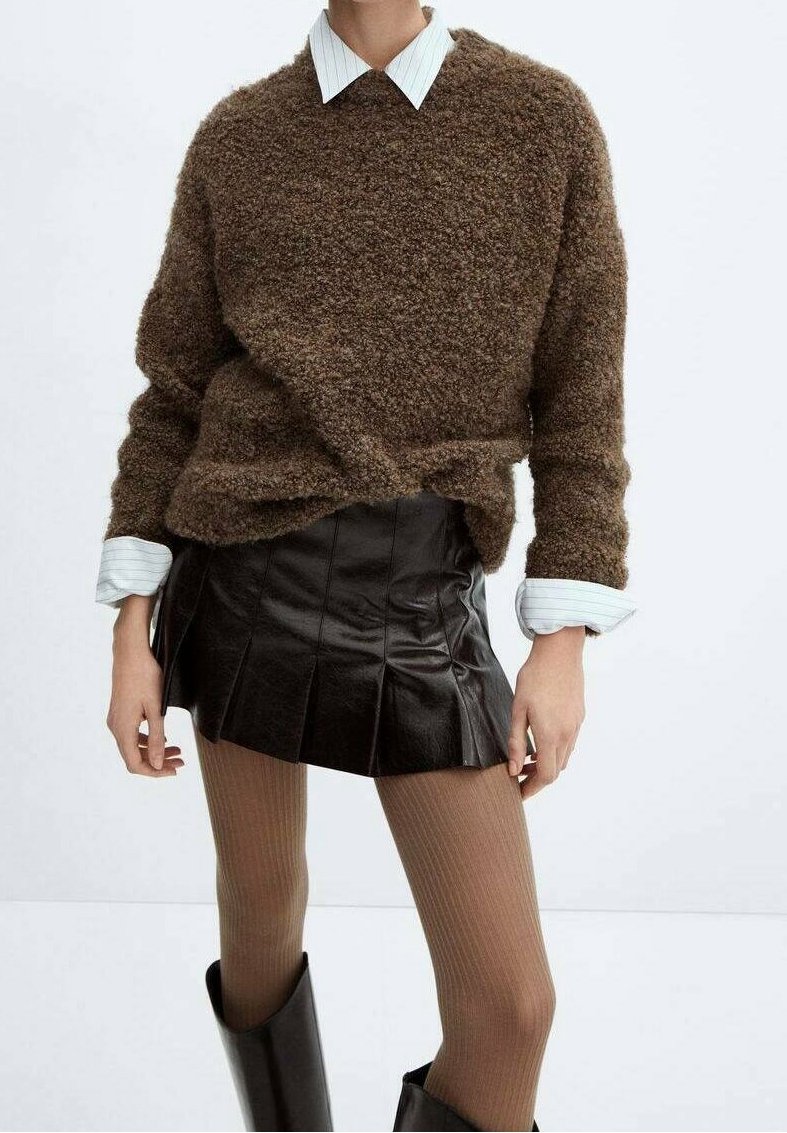 Maglione marrone fluffy sopra una camicia bianca con colletto, abbinato a una gonna plissettata in ecopelle nera e collant a costine beige, completato con stivali al ginocchio.