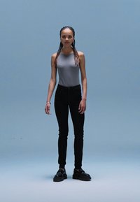 Gray fitted tank top, black skinny jeans, and black platform shoes. Model has long braids. Plain backdrop, focusing on outfit details.