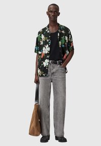 Kwiatowa koszula z krótkim rękawem w czarnym kolorze z zielonymi, czerwonymi i niebieskimi akcentami; zestawiona z jasnoszarymi jeansami o prostych nogawkach i brązową torbą na ramię.