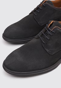 Chaussures en suède noir avec un bout arrondi, un laçage et une surface texturée. Présentent un détail de couture subtil et un intérieur marron contrastant.