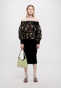 Μαύρο floral μπλουζάκι με γυναικεία γραμμή και φουσκωτά μανίκια, συνδυασμένο με μαύρη μίνι φούστα. Το μοντέλο κρατάει μια ανοιχτό πράσινη τσάντα και φοράει μαύρα πέδιλα με λουράκια.